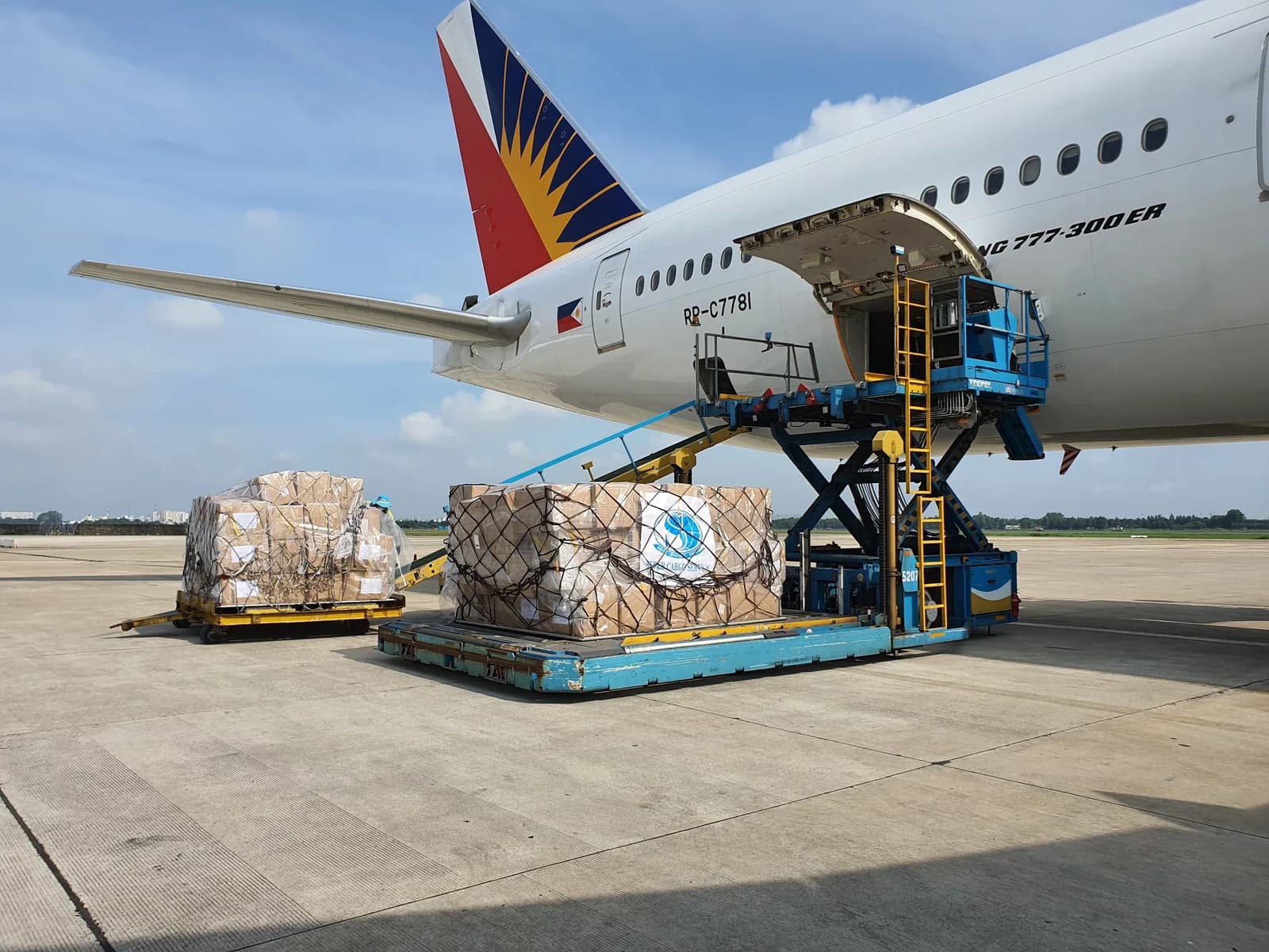 Freight pallets staged on the apron beside a cargo aircraft during daylight loading